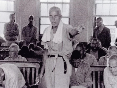 Black and white shot of a man in scrubs at a hospital surrounded by other men with shaved heads
