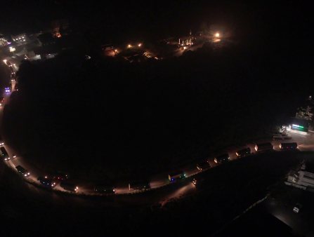Nighttime shot from far above of a winding road full of trucks winding up alongside a hill