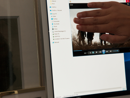 A man's hand is seen covering a video playing on a monitor as a woman's black and white photograph is seen behind it.