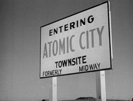 Black and white shot of a sign that reads "Entering Atomic City Townsite Formerly Midway" against a cloudless sky