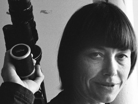 A black and white close-up of a white woman with short dark shoulder-length hair holding a camera