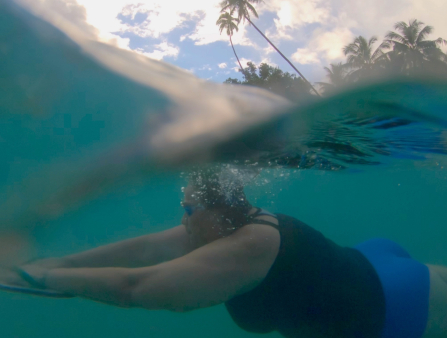 A heavy-set light brown-skinned woman with a one-piece blue suit is seen swimming in the ocean