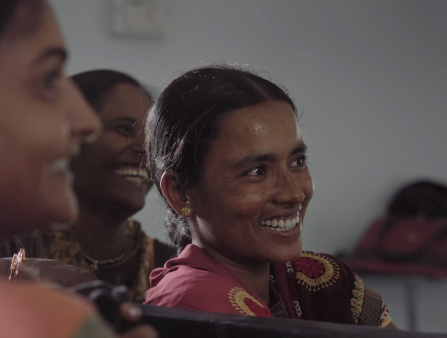 Three Indian women with their hair pulled back smile at something happening right off camera right.