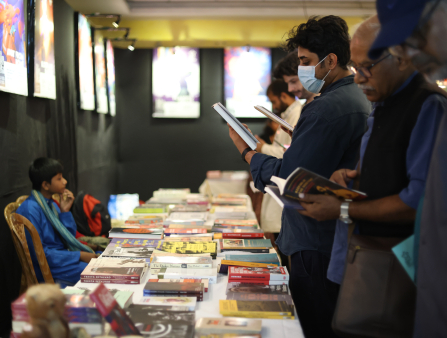 Group of young and old brown-skinned folks (some wearing masks) look at a display of books in front of them arranged in long tables