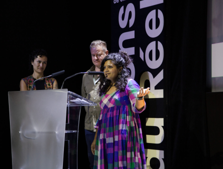 Three filmmakers stand at a metal podium.