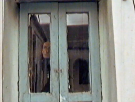 A woman looks out a window framed with wood painted blue