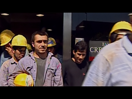 Still from grainy video footage of a group of workers with yellow safety helmets walking toward the camera