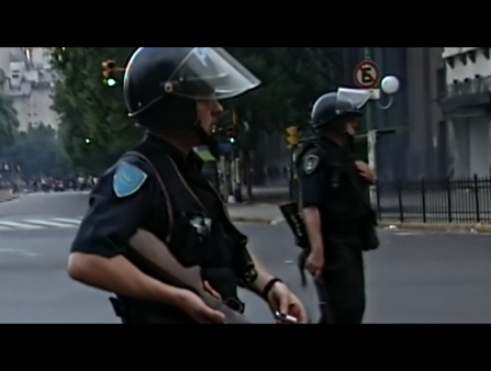 Grainy still of video footage featuring two armed police officers in riot gear walking down an emptied street