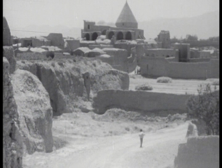 Black and white shot of a sole figure walking a desert road, background dominated by a castle