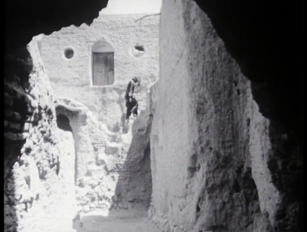 Black and white image of a dark figure walking up the stairs of a ruined castle