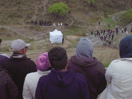 A crowd of people gather on a hill and at the bottom of the hill around a white tent