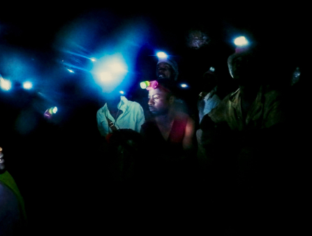 Half a dozen men in vests stand in a pitch black space, the only light source the blue headlamps they all wear