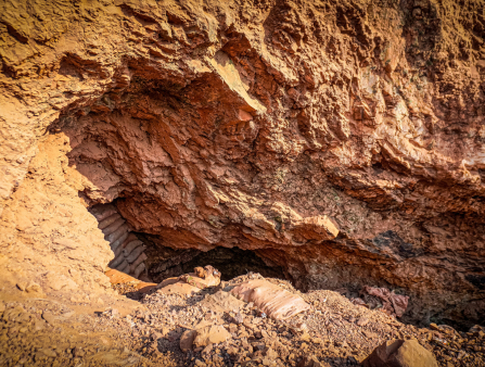 A rough outcropping of orange rock with a cavernous opening