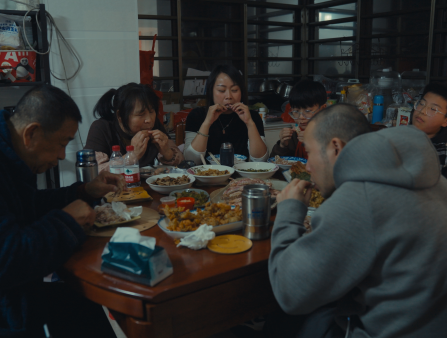 A crowded shot of an Asian family gathered at a round dinner table, all gleefully eating