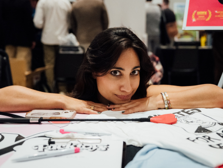 An Indian woman sits at a tabled booth with various film-related knick-knacks