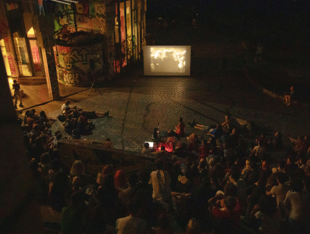 Shot from above a colosseum filled with people watching a screen displaying a black and white film