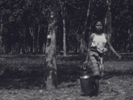Black and white image of a dark-skinned woman carrying a pail of water in a field