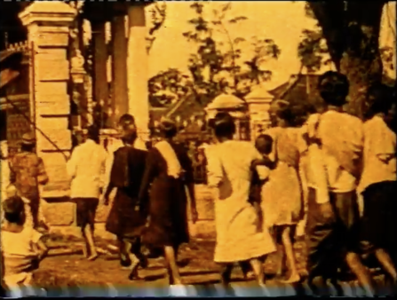 Orange image of a line of people in white and black robes marching through a village