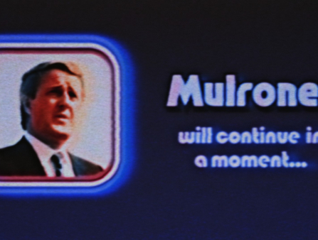 A small square headshot of a man in a suit in front of a white background framed in blue is placed on the lefthand side of the black background. The righthand side contains the text "Mulroney will continue in a moment..." with the word 'Mulroney' significantly bigger than the others