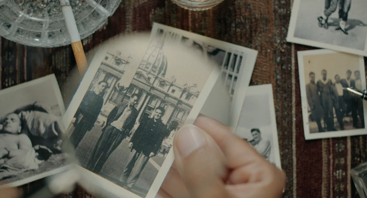 From Victoria Linares Villegas It Runs in the Family. Courtesy of True/False. Hand holding a black and white photo in focus of three people in front of a large statue and building.