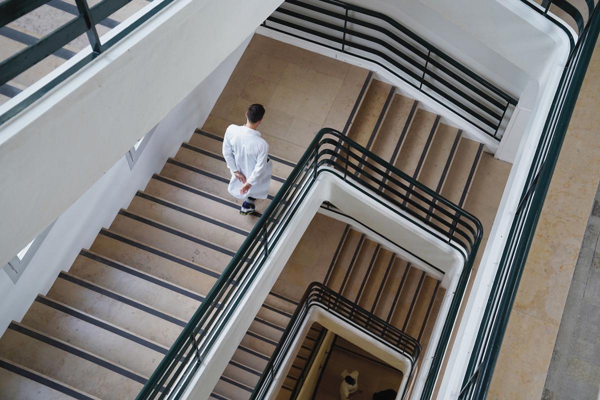 Still from "On the Edge," directed by Nicolas Peduzzi. From overhead, a man in a white doctor's coat descends down a series of stairs.