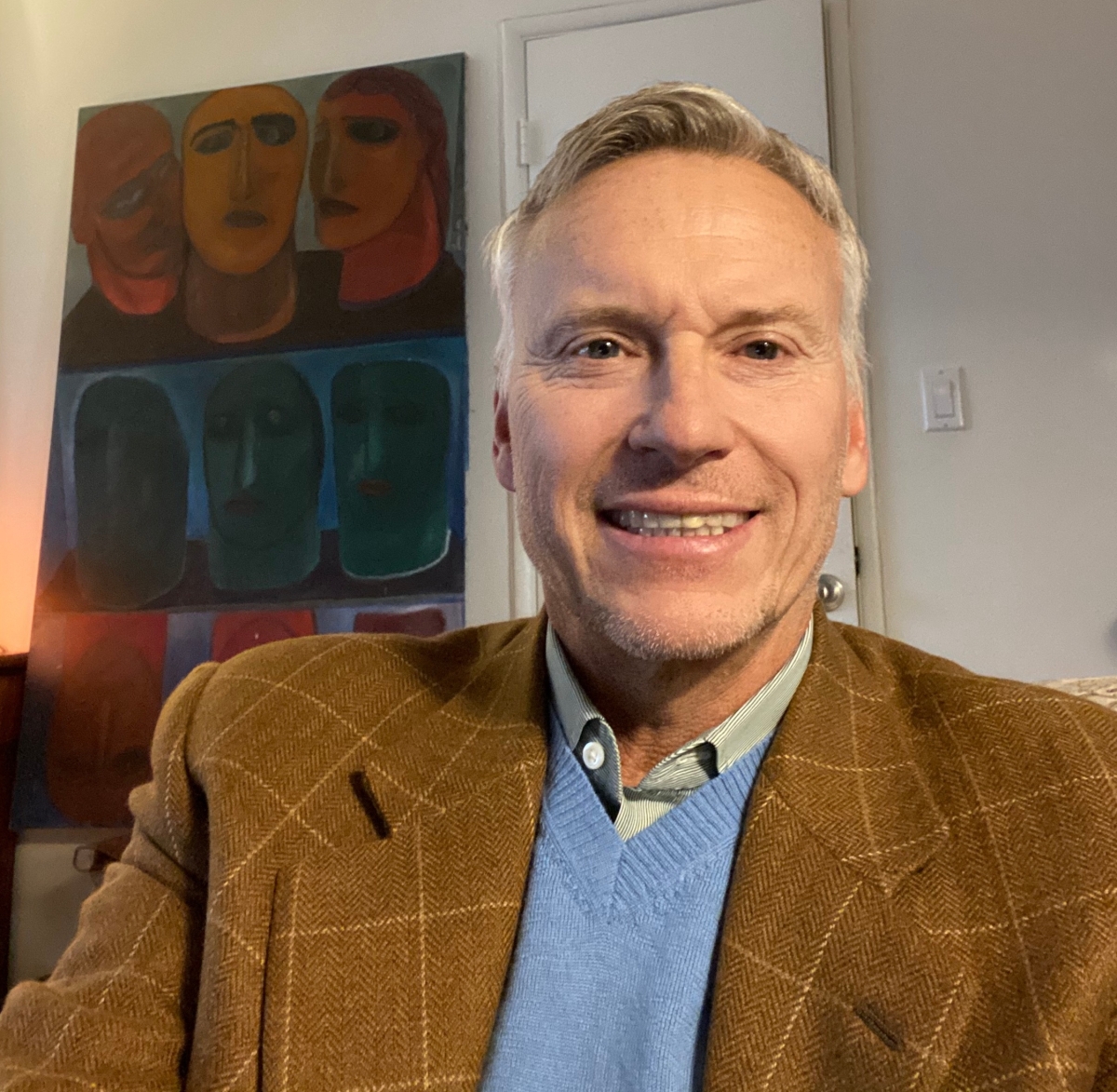 Headshot of a middle-aged male of caucasian descent, short gray-blond hair, wearing a butterscotch sportcoat, blue sweater and green striped shirt. 