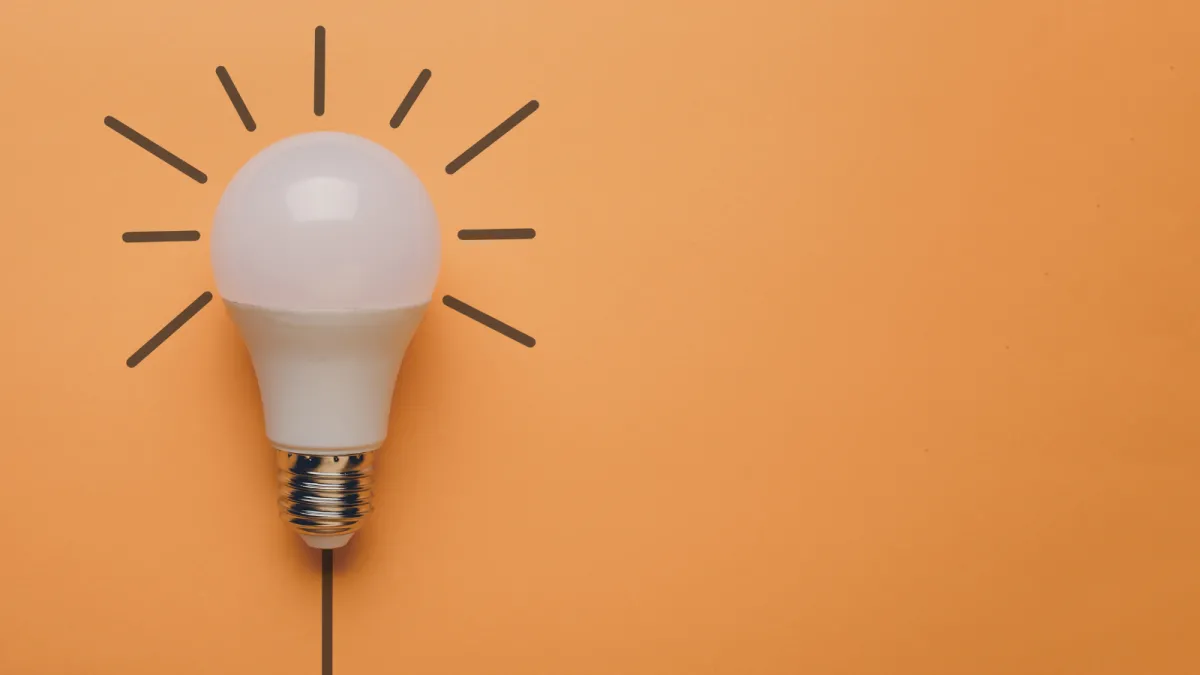 A lightbulb sits on the left side of a soft orange backdrop. Little rays pop out of it, as if they were drawn onto the backdrop. 