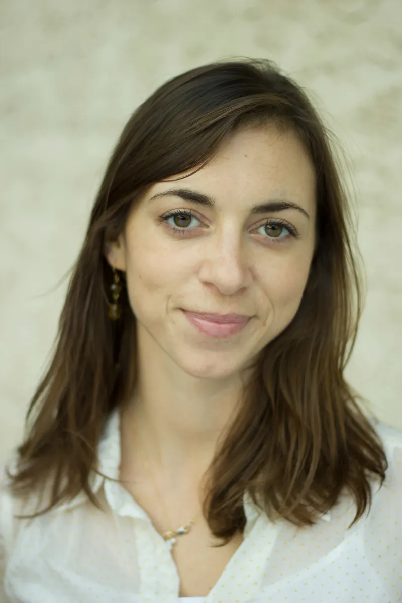 Headshot of a white woman with shoulder length brown hair and brown eyes, wearing a white shirt and brown earrings.