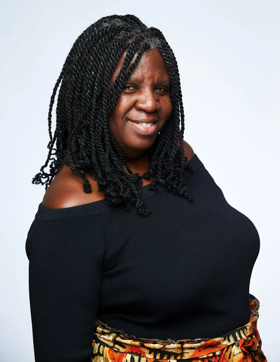 Black woman with black, shoulder-length braids, wearing a black off-the-shoulder long sleeve shirt.