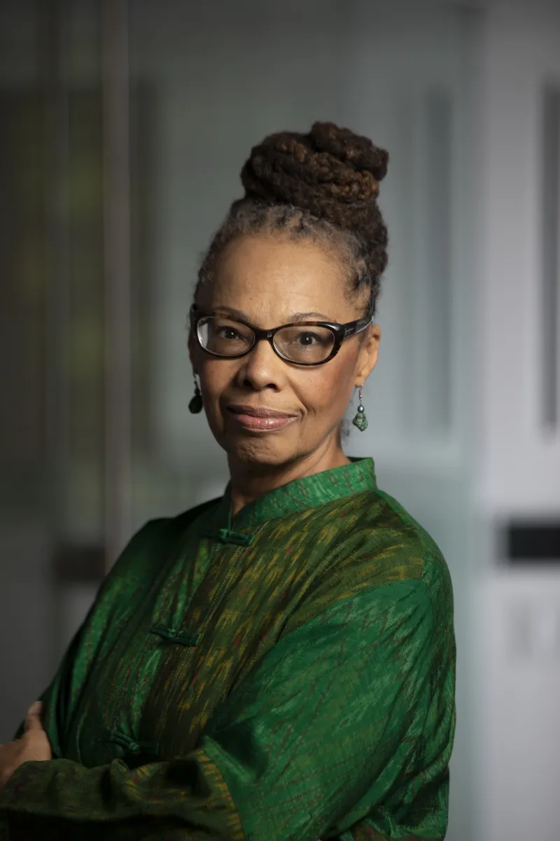 Black woman with brown hair in a bun, wearing glasses and a green long-sleeve top.