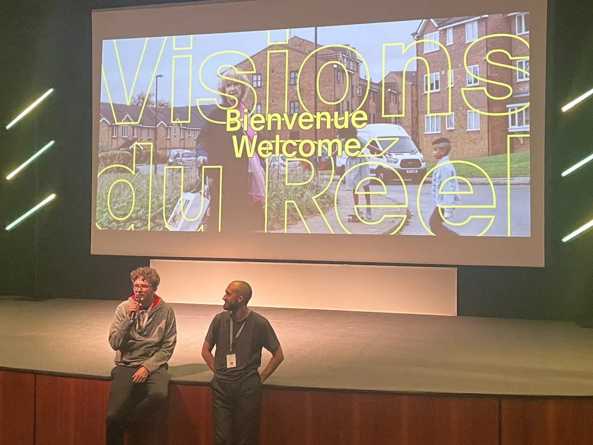 Screen of a welcome sign for Visions du Réel. Two men standing in front of the screen, one on left is 'Pianoforte' director, Jakub Piatek.