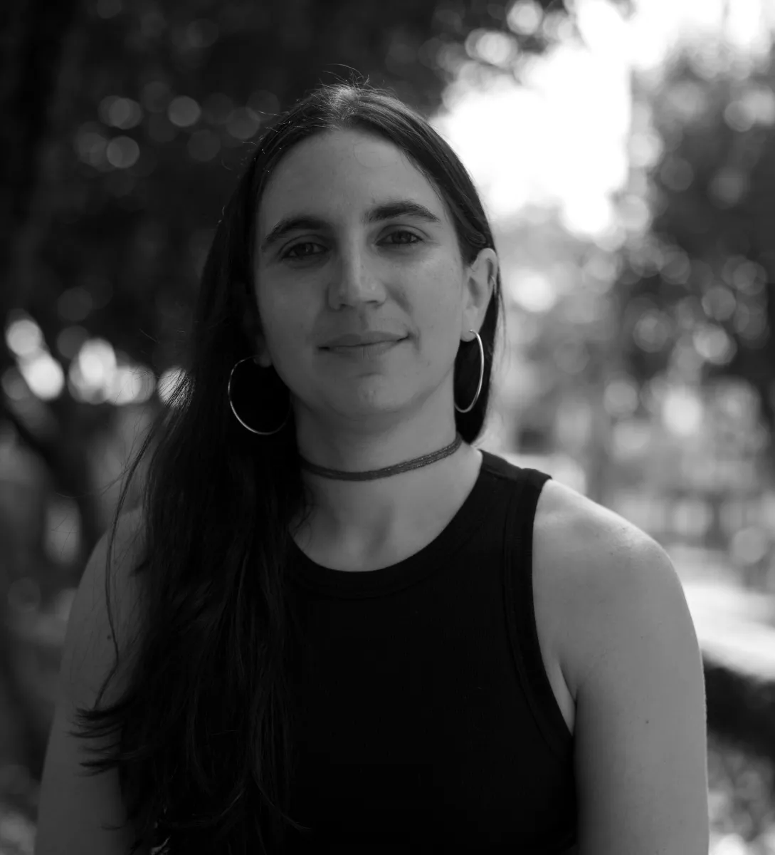 Screenshot of a middle age woman of latin American descent, behind a garden with trees