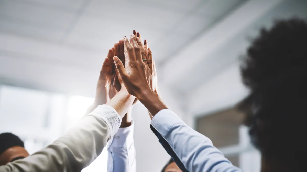 People in a circle. Their hands raised, touching in the center.