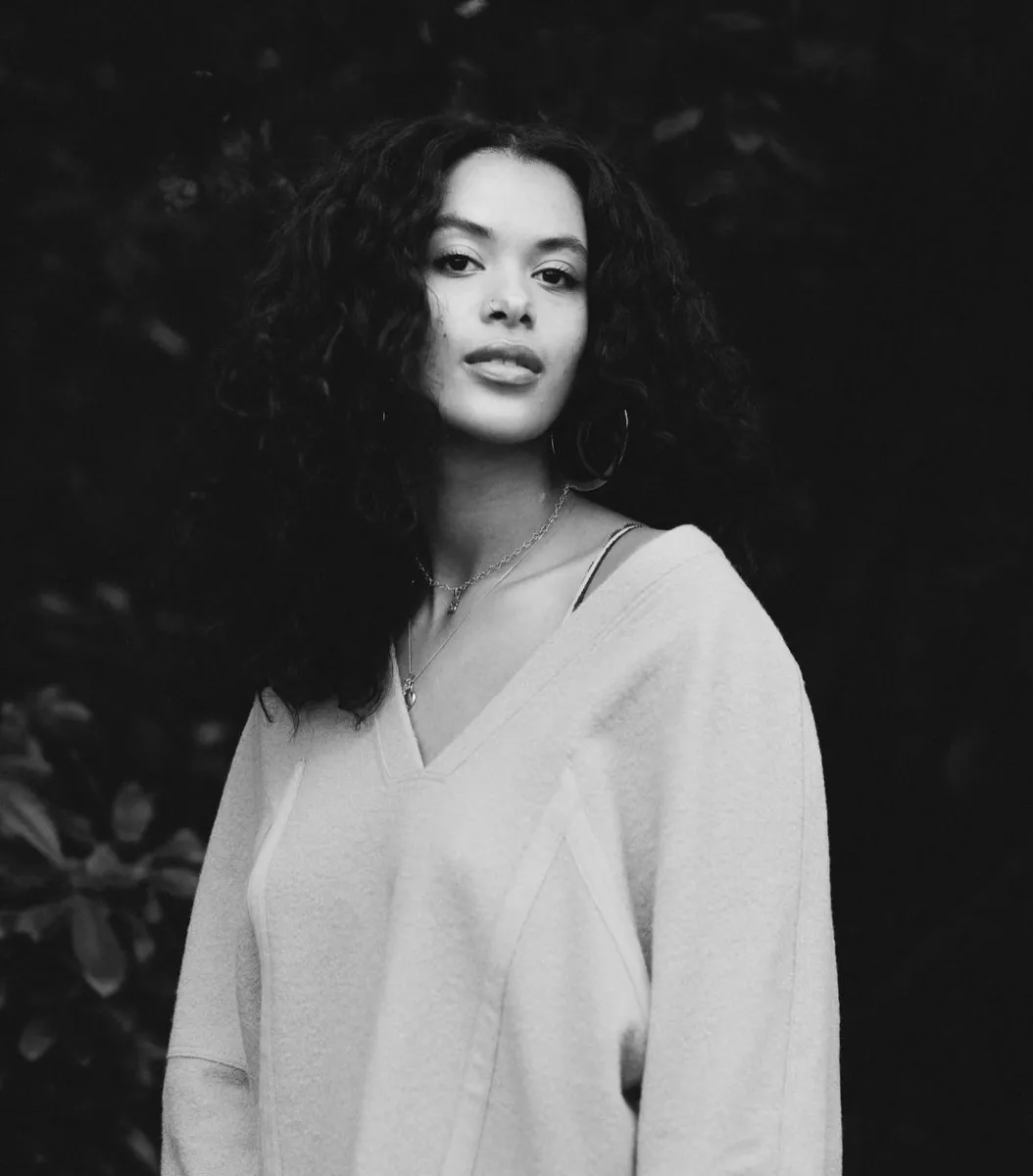 Headshot of a Black woman with in a tunic with long curly brown hair, photo is in black and white.