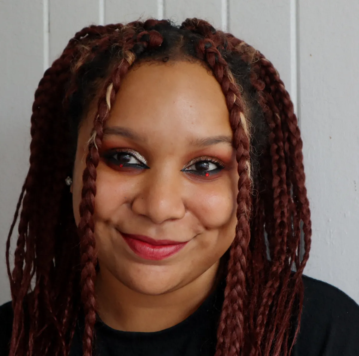 Headshot face and top of shoulders of an adult with medium-light skin tone, red braided hair in two ponytails with two braids framing face, smiling