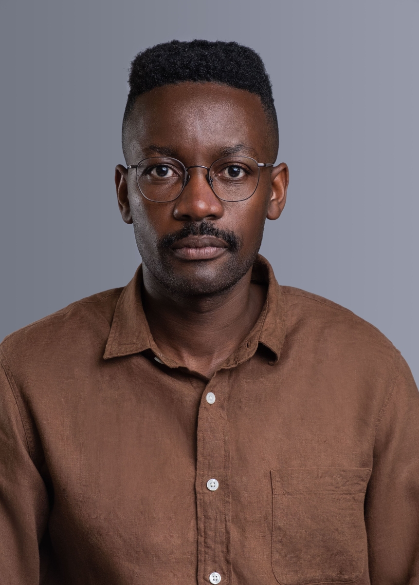 Headshot of a middle-aged male of African descent in a brown shirt, in front of a white background