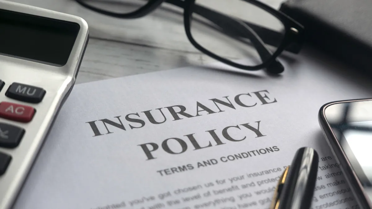 An image with a letter that reads Insurance Policy on top of a desk with glasses and a calculator