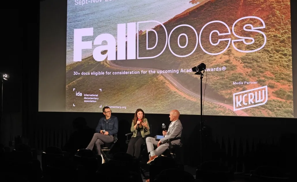 Two men and a woman in front of a projector screen speaking into microphones