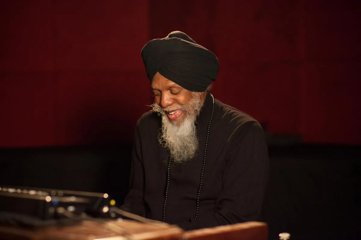 A man with a long beard, wearing dark attire and a turban, playing an organ