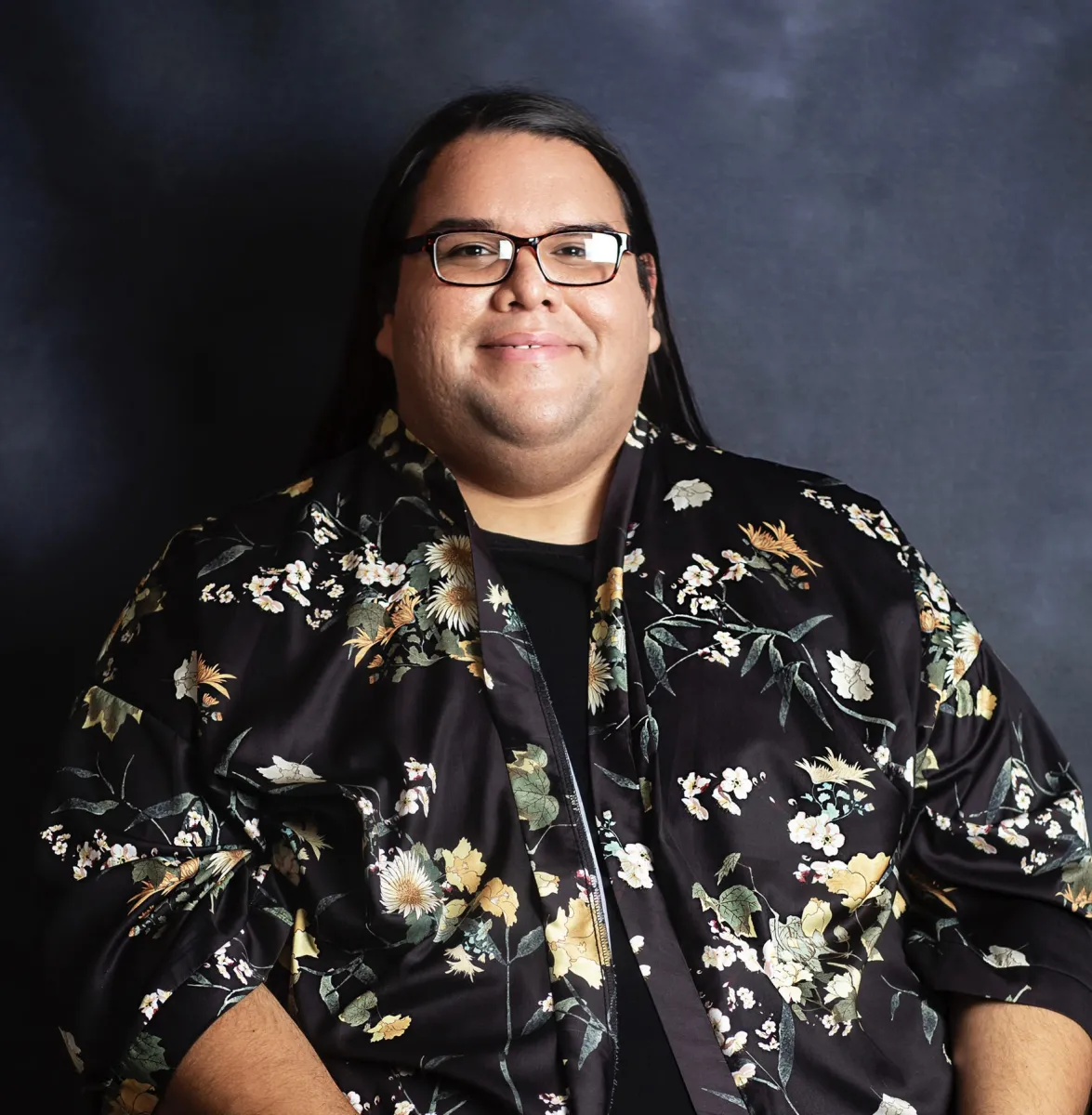 headshot of Ivan MacDonald wearing a black top with flowers and black glasses