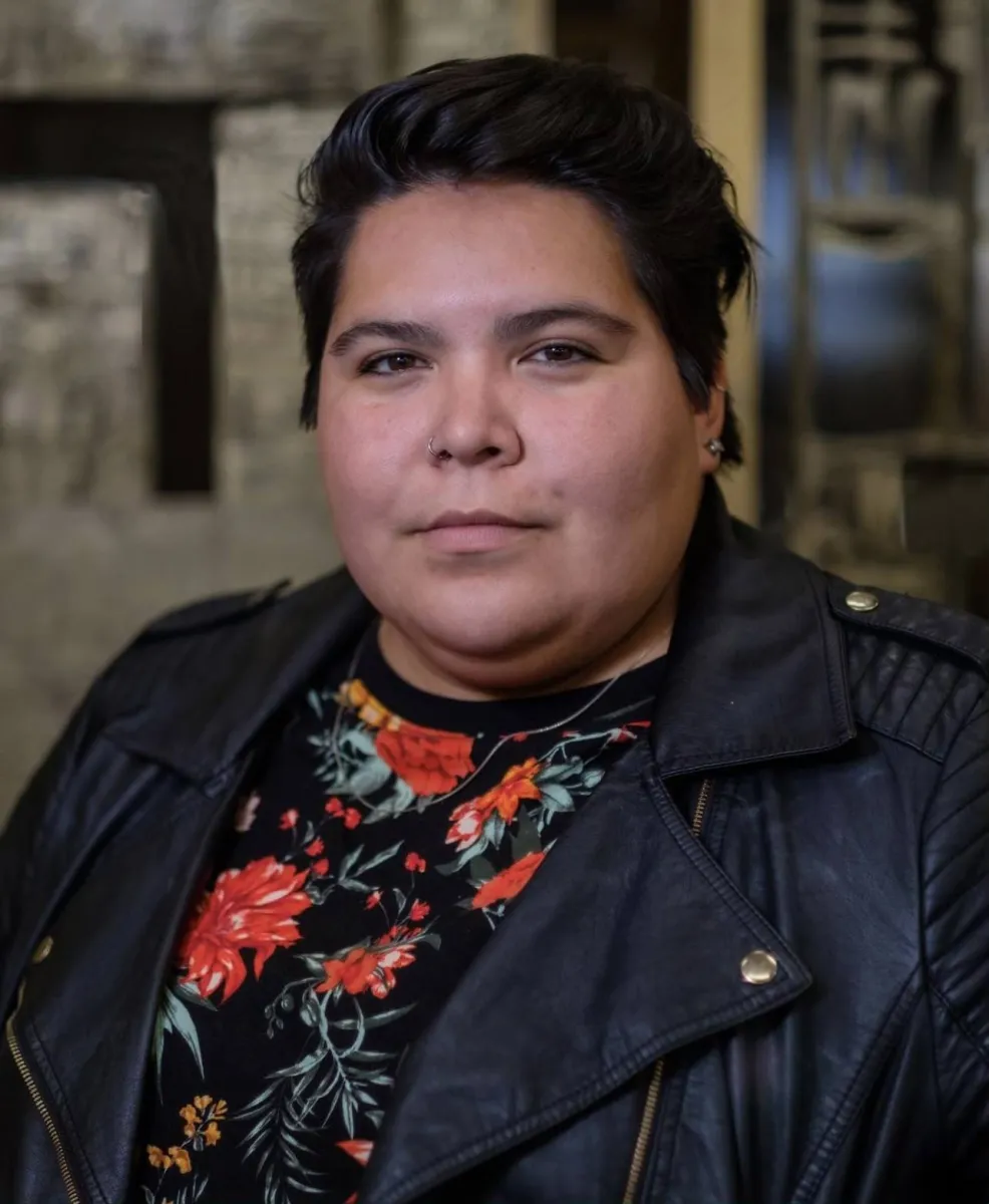 headshot of Ivy MacDonald wearing a black leather jacket with a black shirt with red flowers