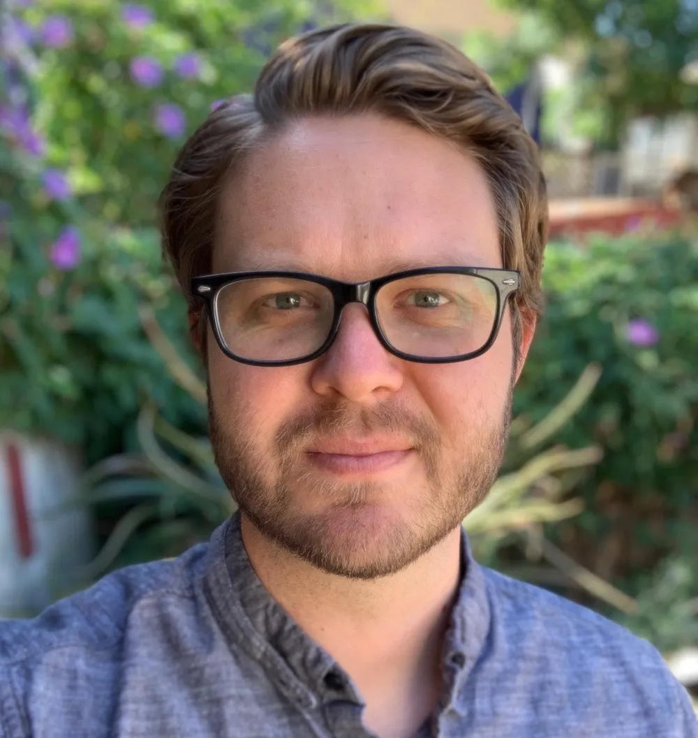 headshot of Lucas Guilkey wearing a blue shirt and black glasses