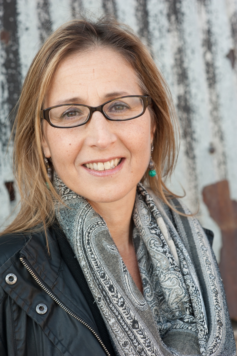 headshot of Lorena Luciano wearing a gray scarf with a black leather jacket and black glasses