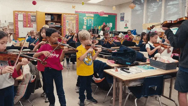 A music teacher instructs a classroom full of second graders holding violins.