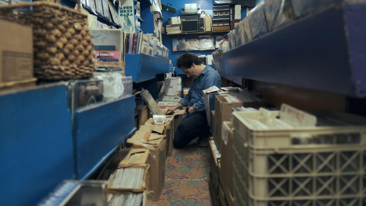 A white man flips through crates of records while kneeling on the ground.