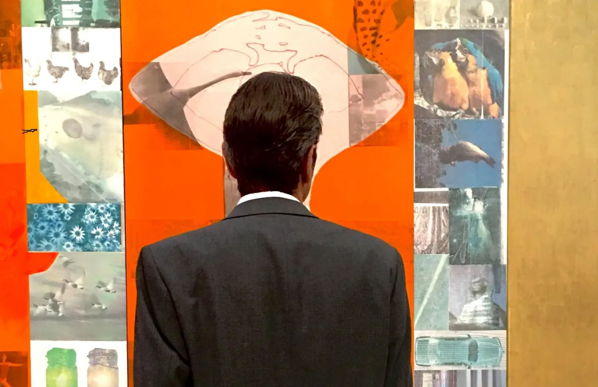 The back of a man in a suit as he stands in front of colorful artwork