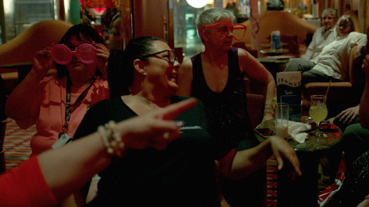 A group of middle-aged women dance in a dimly-lit bar.