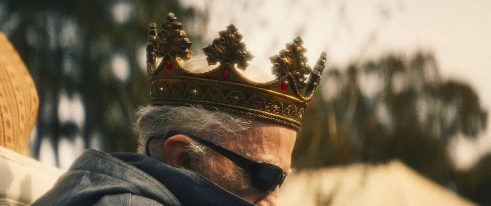 A profile view of a man wearing a crown and sunglasses.