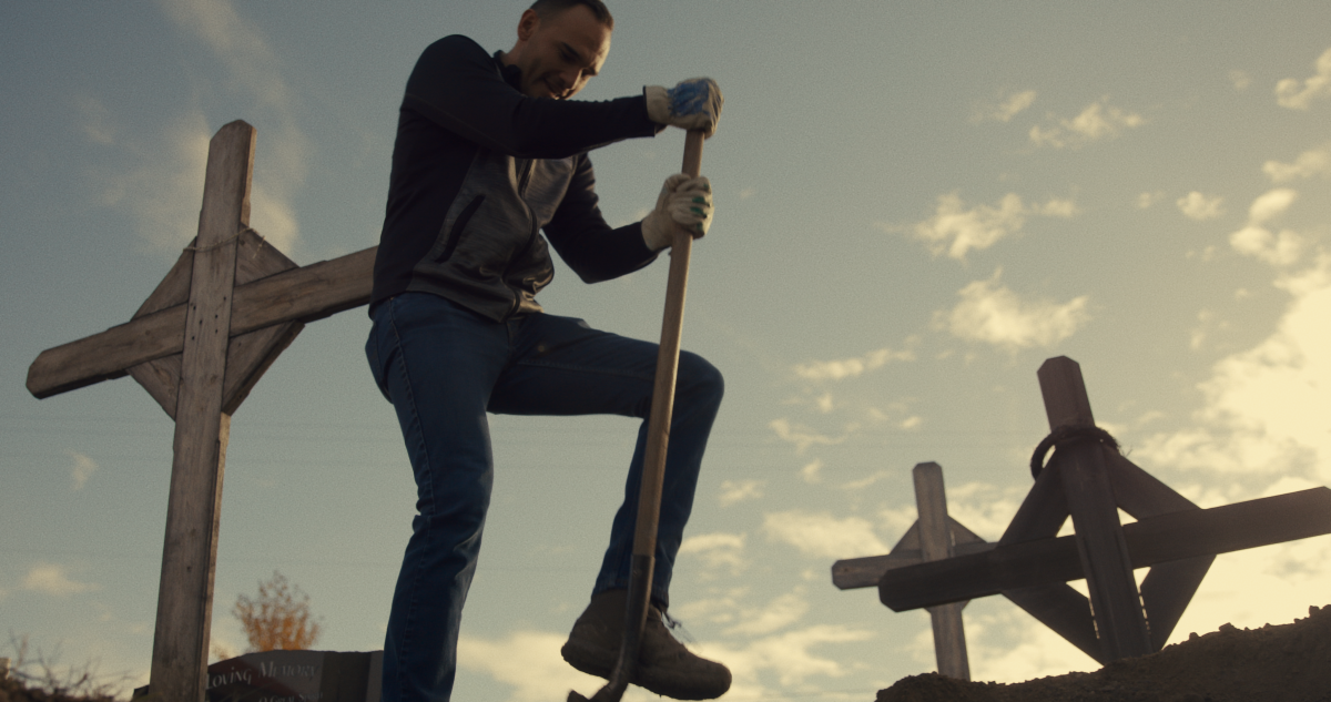 From below, a man digs a grave.