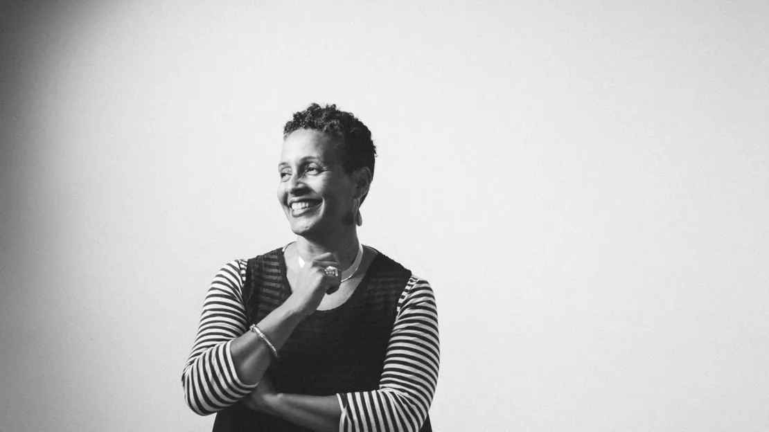 A black and white photograph of a smiling Black woman with short hair. She is wearing a dress with striped sleeves.